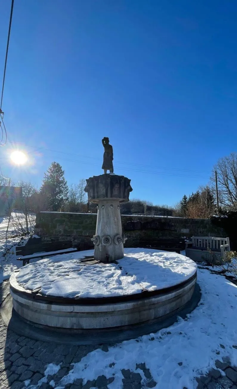 Der Zöllmener Dorfbrunnen im Winter: folkloristisch gestalteter Zierbrunnen von Eberhard Wolf aus dem Jahr 1989, direkt an der Grundstücksauffahrt Am Erlengrund 6.