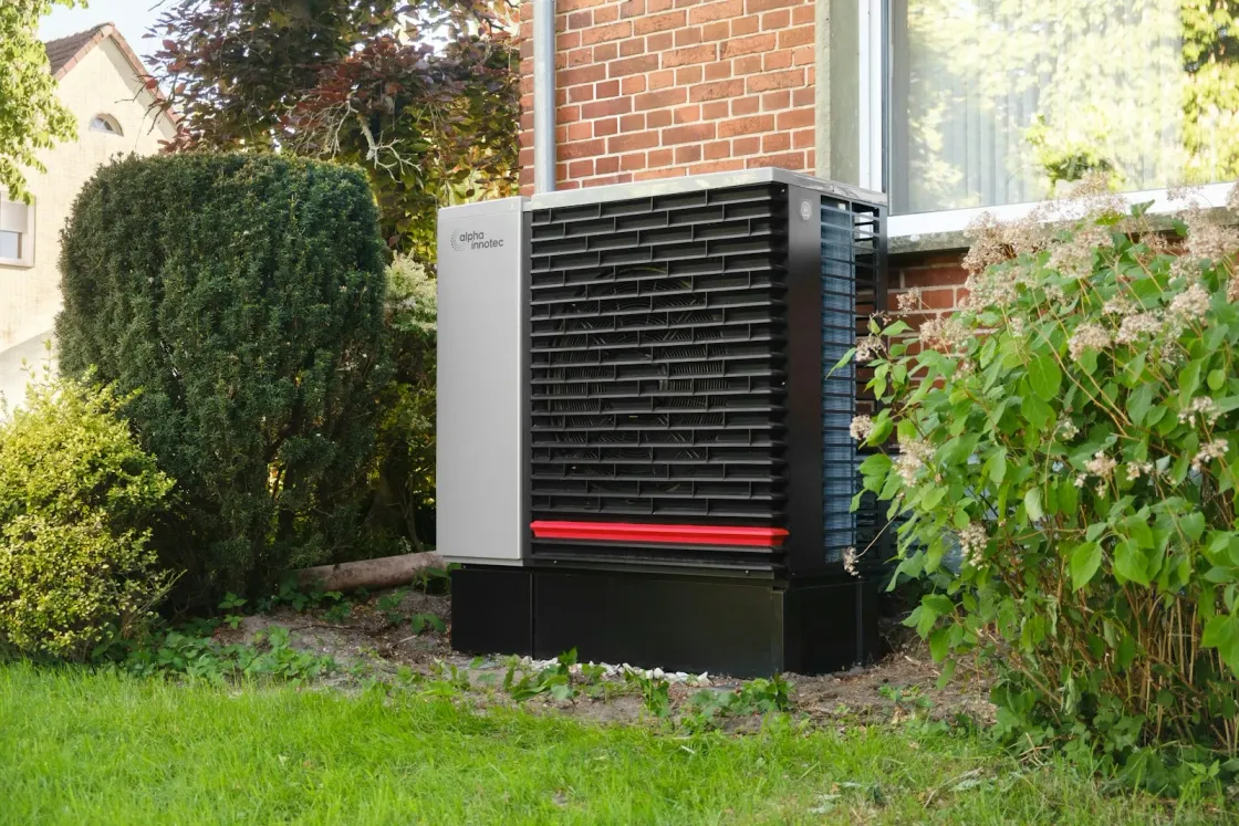 Wärmepumpe im Garten eines Backsteinhauses – der Umstieg im Altbau wird 2026 weiterhin staatlich gefördert