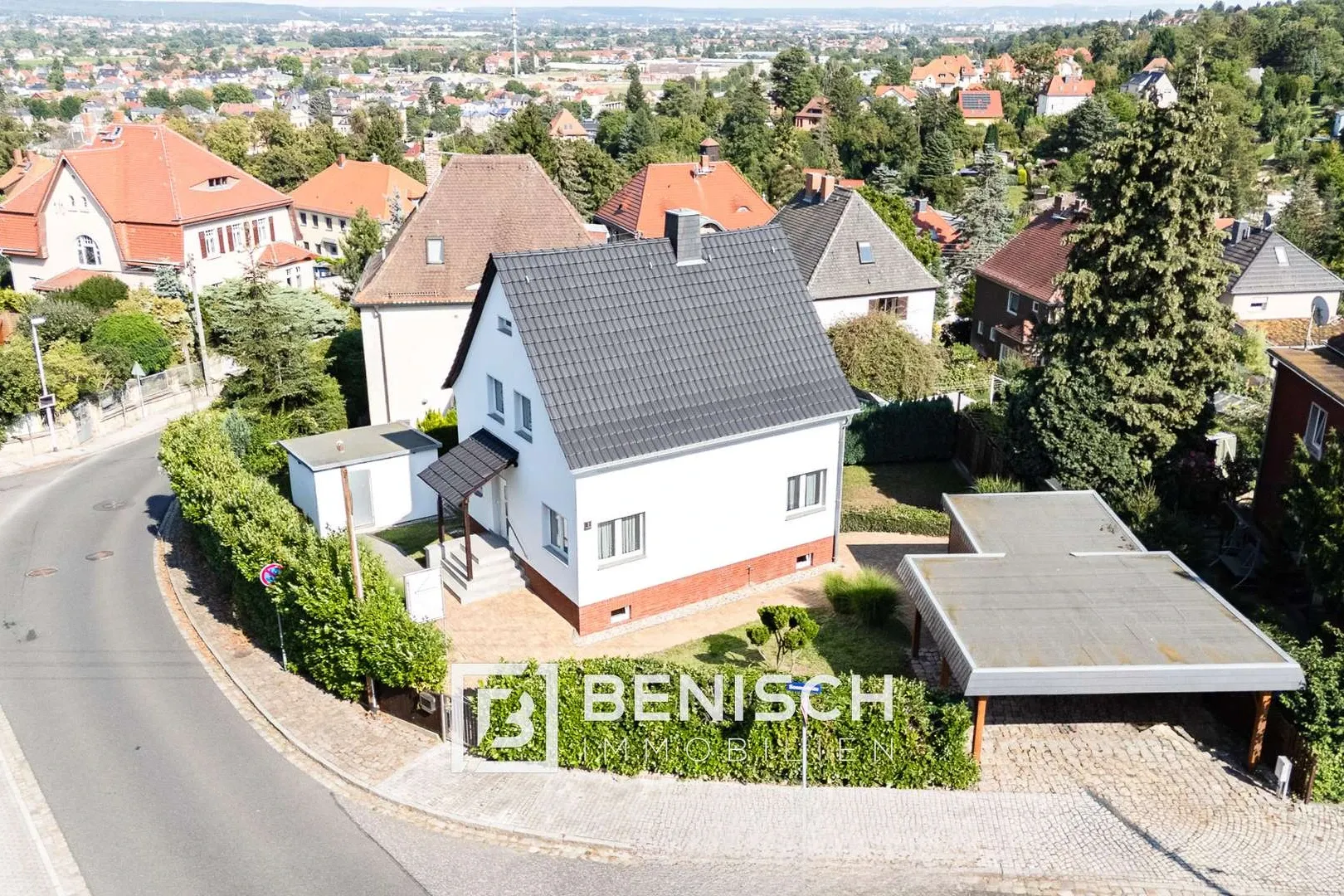 Von Benisch Immobilien verkauftes Einfamilienhaus in Dresden – weiß verputzter Bau mit dunklem Satteldach, Klinkersockel und Carport