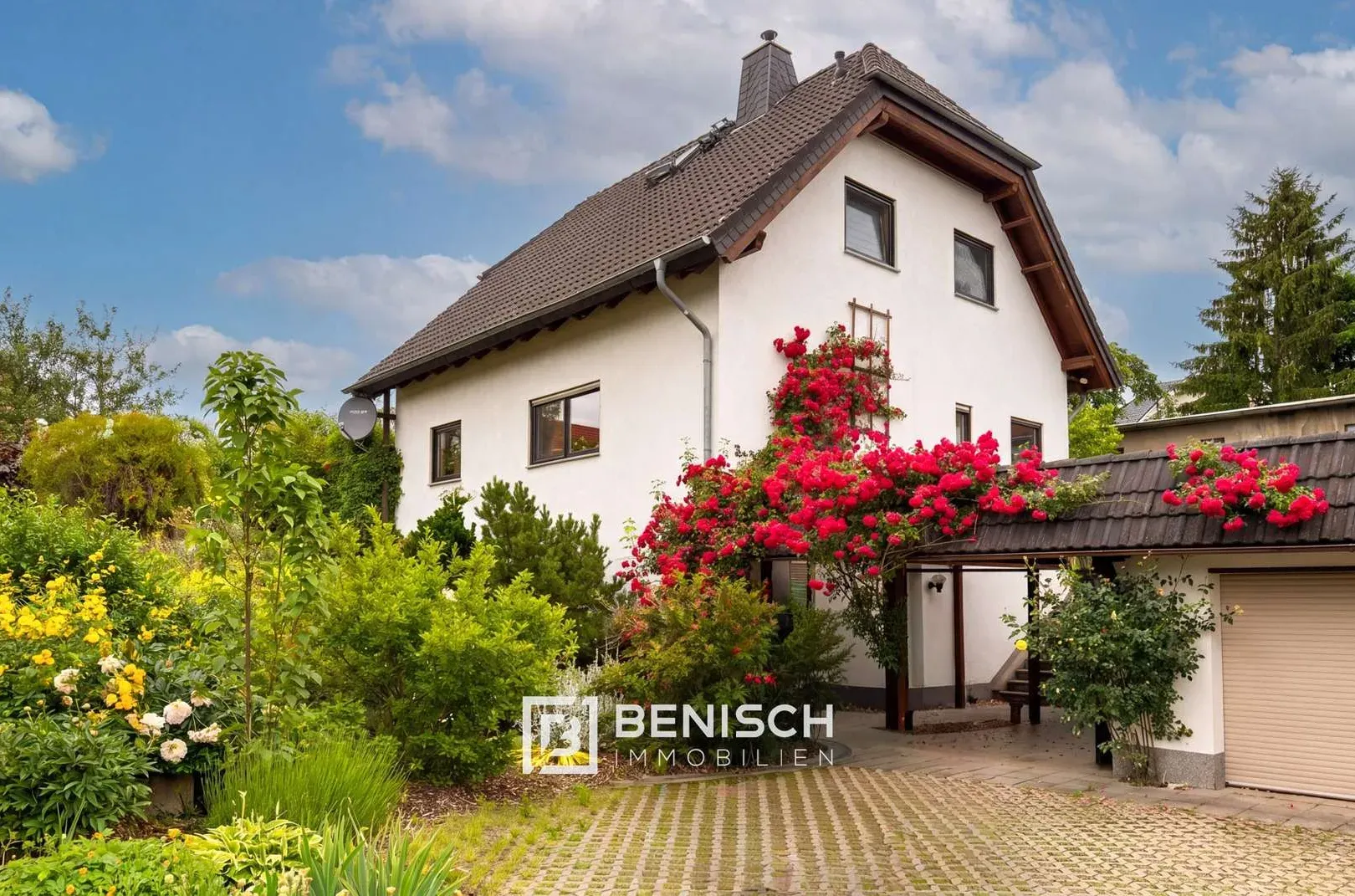 Von Benisch Immobilien verkauftes Einfamilienhaus im Dresdner Umland – weißes Haus mit dunklem Satteldach, Kletterrosen an der Fassade, Garage und gepflasterter Einfahrt