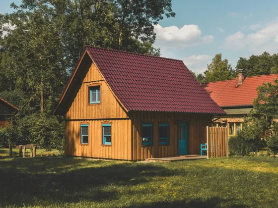 Freistehendes Holzhaus mit rotem Satteldach auf einer Rasenfläche zwischen Bäumen