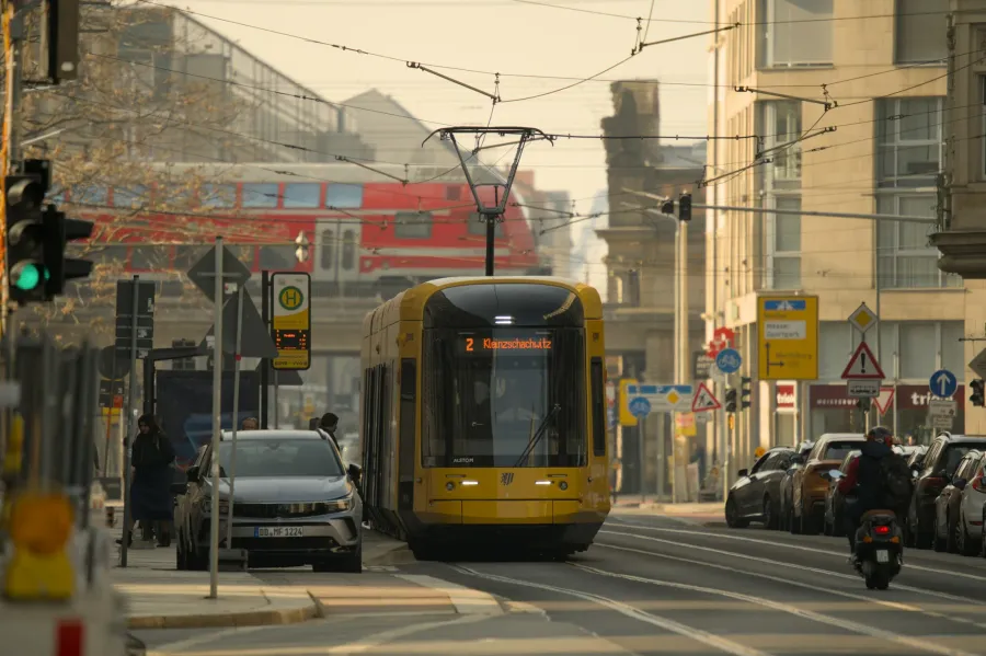 Gelbe Straßenbahn, Autos und ein Zug auf einer breiten innerstädtischen Hauptstraße in Dresden – dichter Verkehr direkt vor den Wohnhäusern.