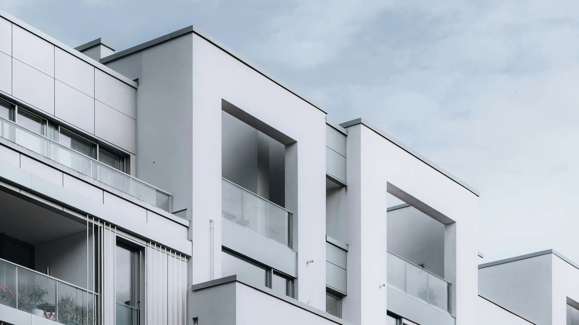 Moderne Neubau-Architektur: helle Putzfassaden mit tiefen Loggien und Glasbrüstungen vor bedecktem Himmel – Symbolbild