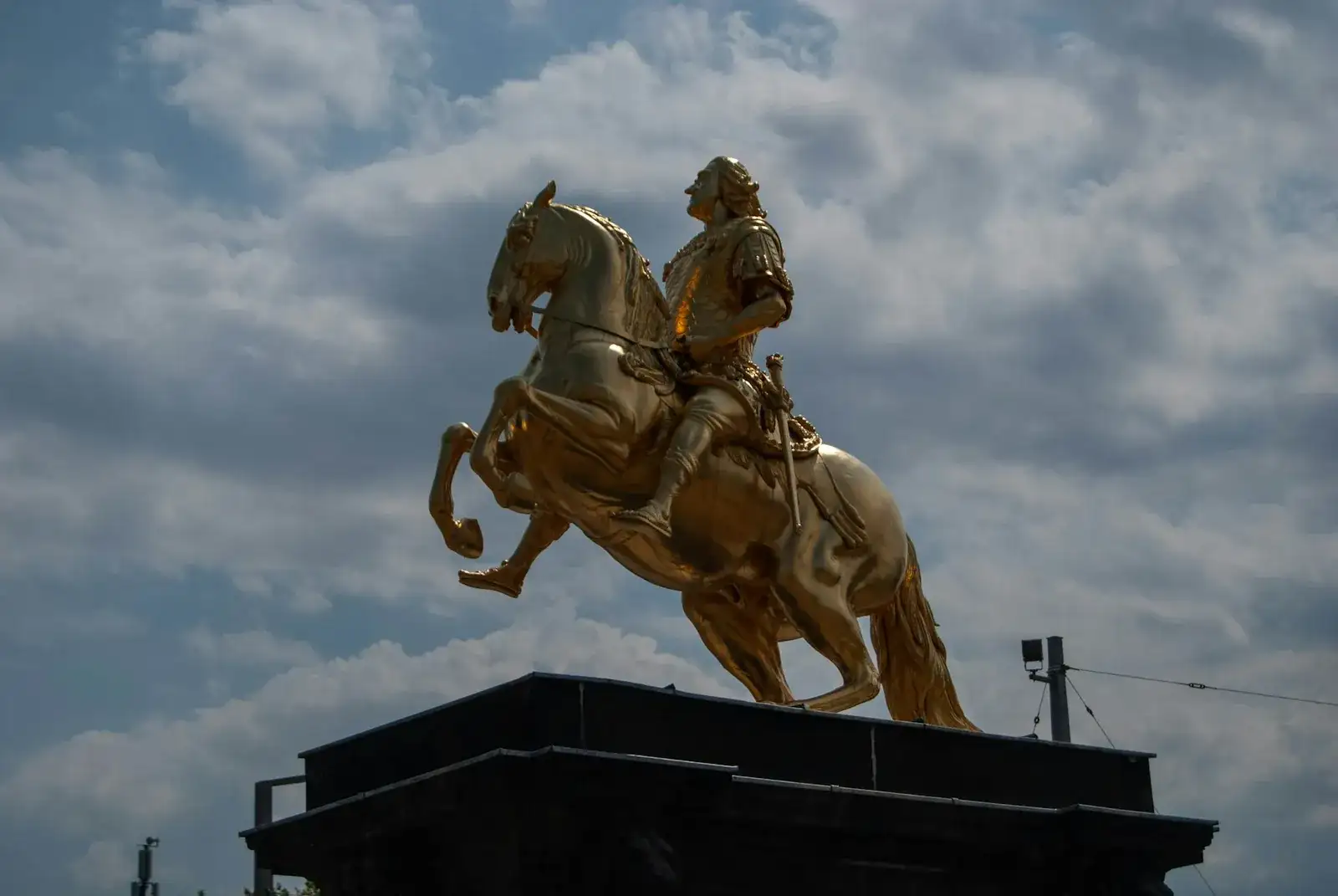 Der Goldene Reiter, das vergoldete Reiterstandbild Augusts des Starken mit steigendem Pferd, leuchtet in warmem Gold vor blauem Wolkenhimmel im Barockviertel der Inneren Neustadt in Dresden.