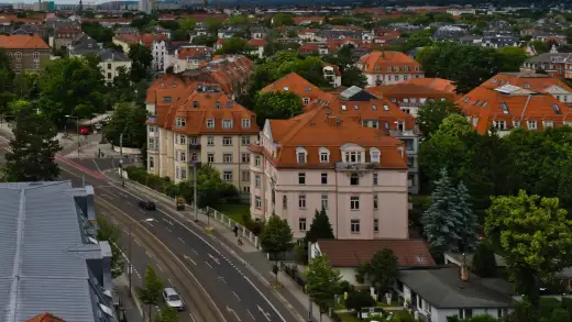 Blick vom Ernemannturm über Dresden-Striesen Richtung Pohlandplatz: Stadtvillen und Mietshäuser mit roten Ziegeldächern zwischen hohen Bäumen, vorn eine Straße mit Straßenbahngleisen.