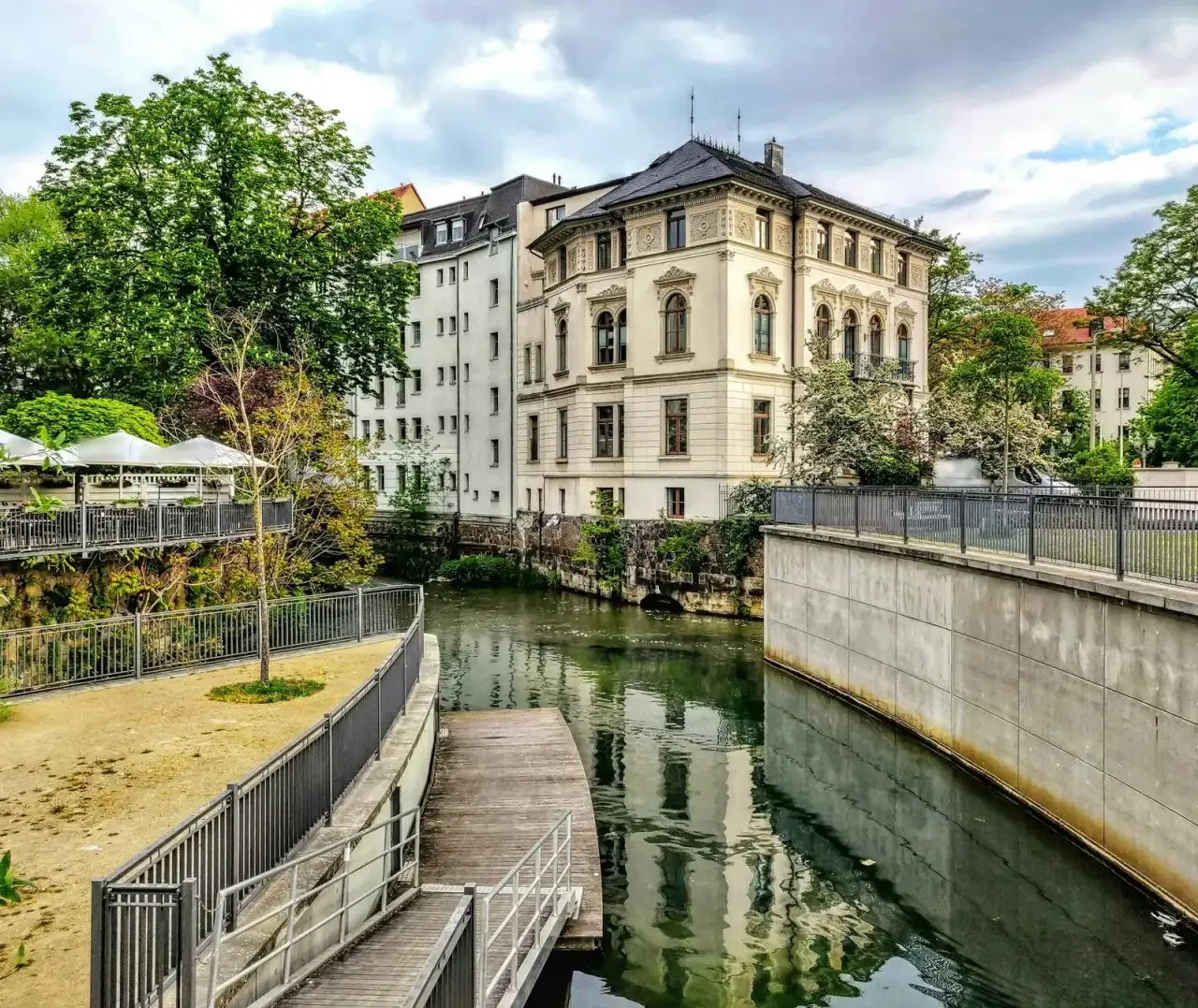 Sanierte Gründerzeitvilla mit Stuckfassade an einem Kanal in Leipzig, davor Bäume und ein Steg