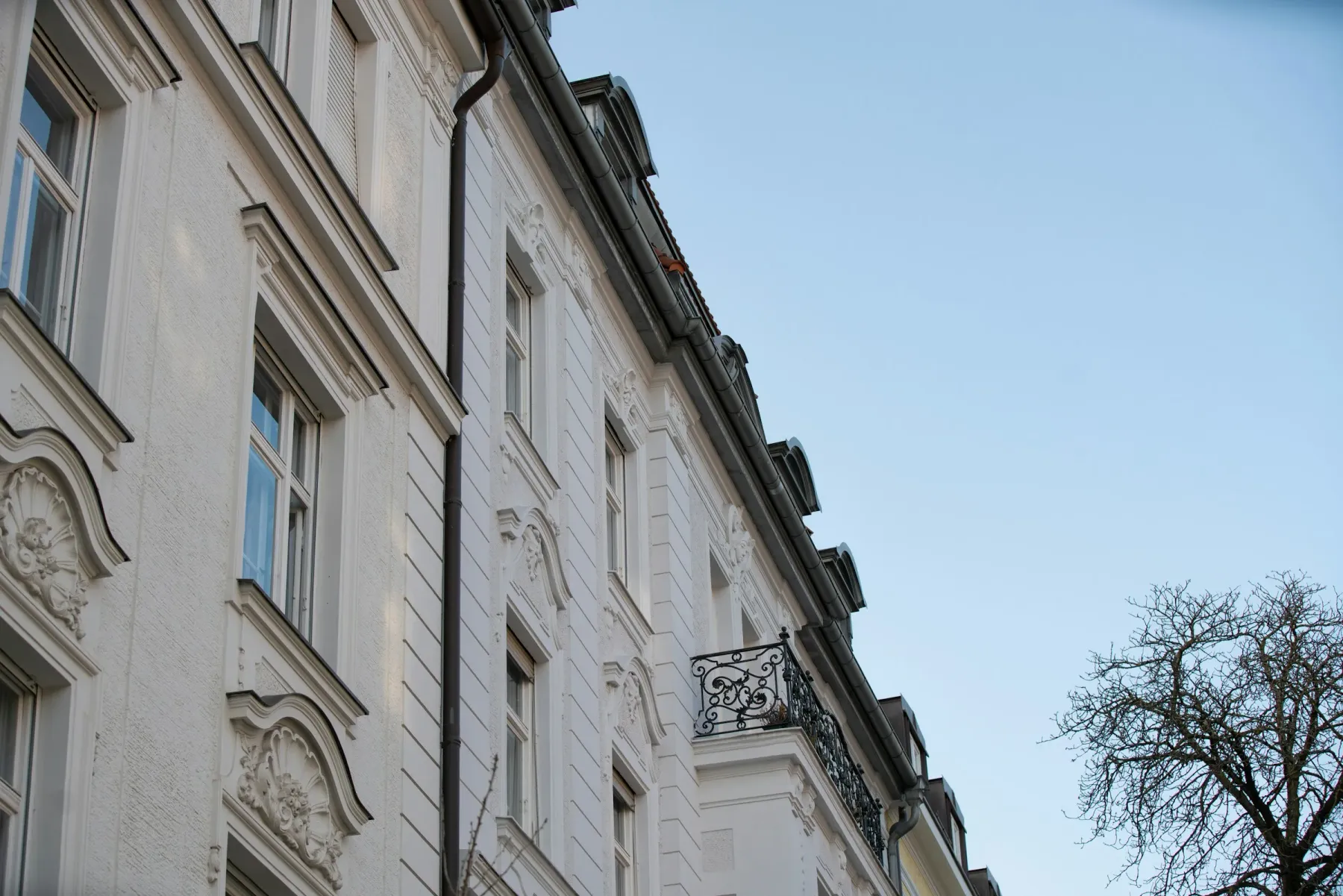 Helle Gründerzeitfassade mit Stuck und schmiedeeisernem Balkon unter blauem Himmel