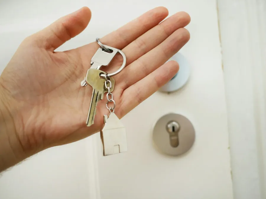Offene Hand mit Wohnungsschlüssel vor einer weißen Wohnungstür – Schlüsselübergabe beim Verkauf